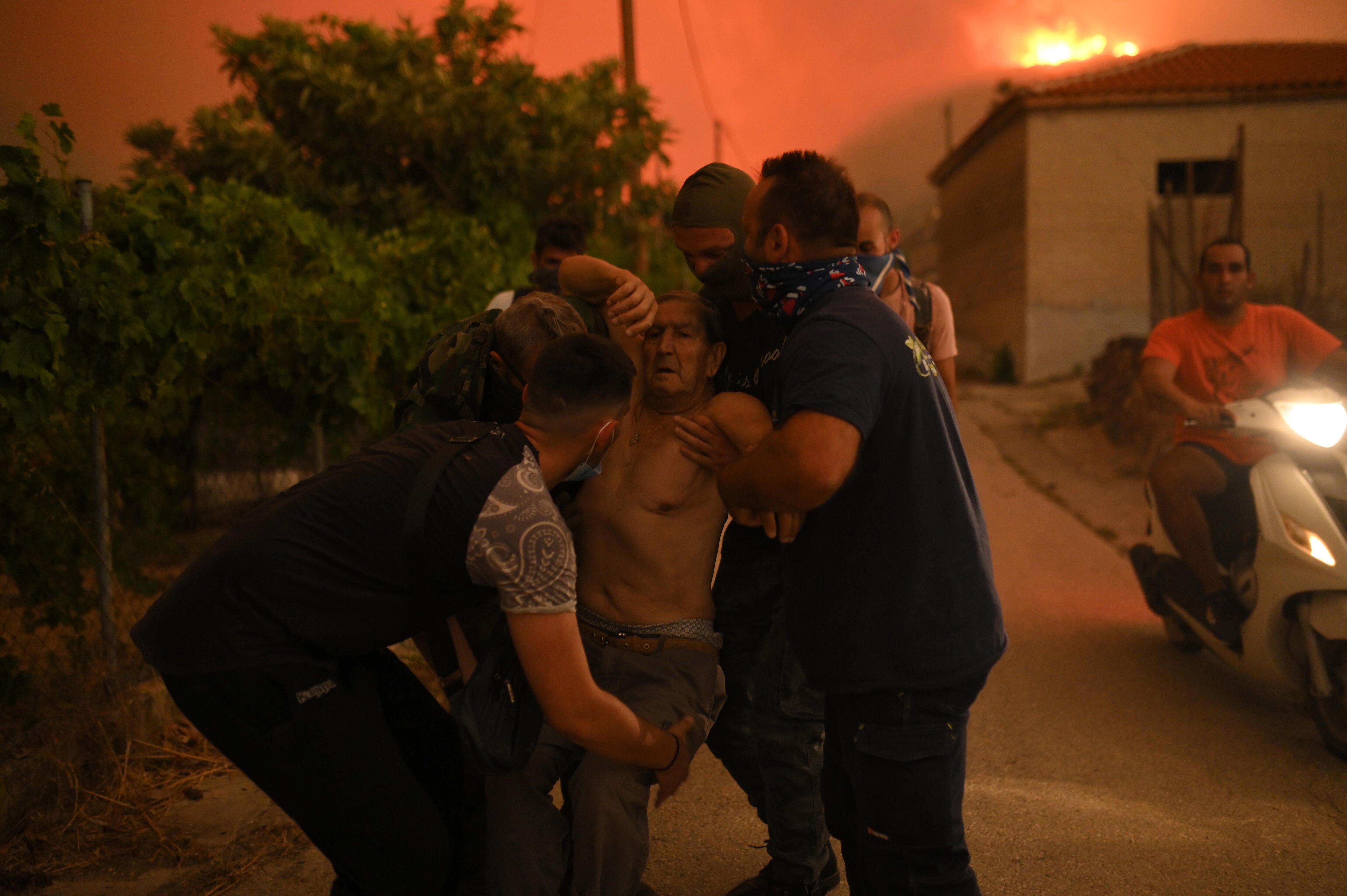 Varios voluntarios asisten a un hombre durante los incendios en Grecia, el lunes 21 de agosto. 
