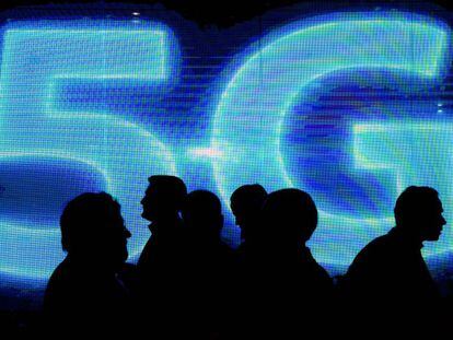Varias personas pasan junto a un logo luminoso de 5G en el &uacute;ltimo Mobile World Congress, en Barcelona.