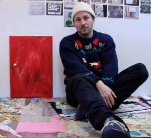 Mike Swaney sentado y apoyado sobre su obra, 'Hut 1 Paintings 4'.