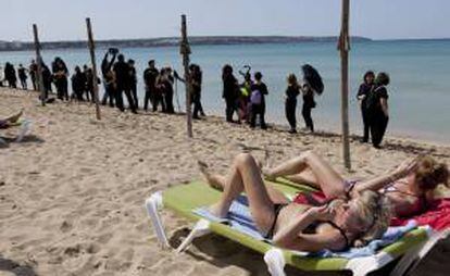 Unos turistas toman el sol ante un grupo de personas de las que han formado en la Playa de Palma una cadena humana en contra de las prospecciones en el mediterráneo.