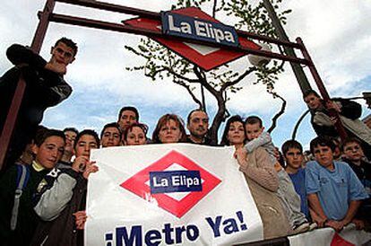 Un grupo de vecinos de La Elipa, debajo de una falsa entrada, muestra una pancarta en la que piden una línea de metro para su barrio.