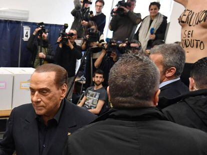 Berlusconi se da media vuelta, mientras una activista de Femen protesta con la frase escrita en su pecho "estás acabado".
