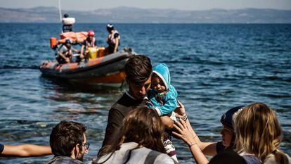 Varios voluntarios ayudan a un inmigrante afgano tras llegar con un bebé a la isla de Lesbos.