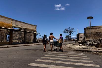 Unos residentes transportan un carrito entre las ruinas de los edificios quemados por el incendio, este viernes en Lahaina (Hawái). 
