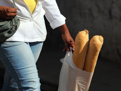 Una mujer camina con dos barras de pan en una bolsa de pl&aacute;stico.