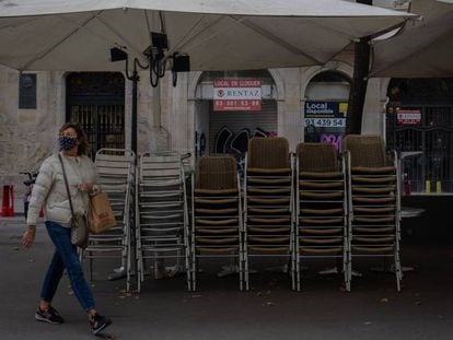 Una mujer pasa junto a la terraza recogida de un bar cerrado durante la entrada en vigor de las nuevas restricciones en Barcelona, Cataluña 