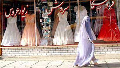 Una joven afgana pasa frente a un escaparate de vestidos de novia de colores blanco, rosa y rojo que se alquilan en Kabul.