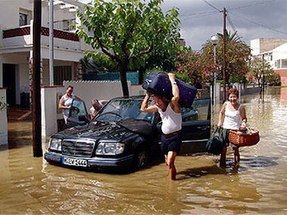 Una familia extranjera intenta extraer sus pertenencias del vehículo en una calle de Coma-ruga inundada por la lluvia.
