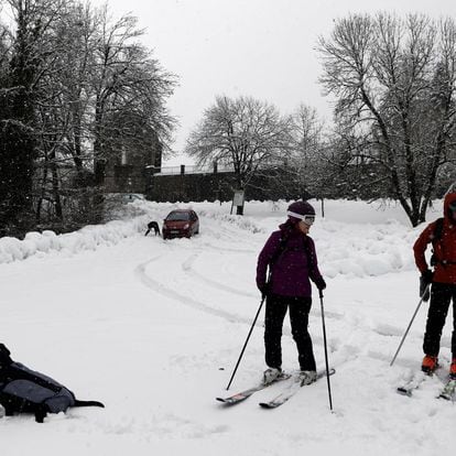 Dos esquiadores junto a un perro disfrutan entre la nieve del aparcamiento parking de Roncesvalles completamente cubierto.