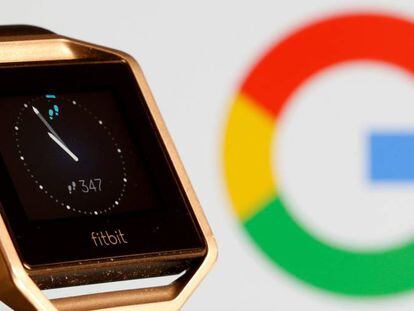 Reloj de la compañía Fitbit frente a una pantalla con el logotipo de Google.