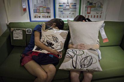 Dos chicas, sujetan unos cojines, mientras descansan en un sofá del Ikea.