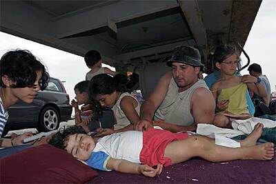 Mohamed y su familia se protegen del sol bajo un camión aparcado ayer en el puerto de Almería, donde miles de personas esperaban.