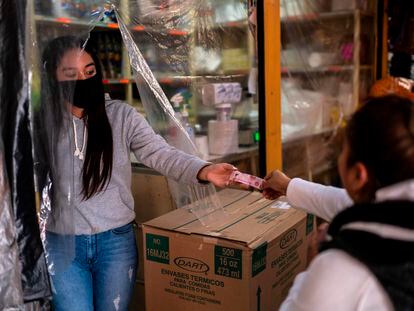Una vendedora recibe dinero detrás de un plástico en un negocio de México.