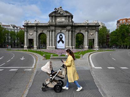 Una mujee con un carrito de bebé pasa ante la Puerta de Alcalá de Madrid, con un lazo negro en señal de duelo.