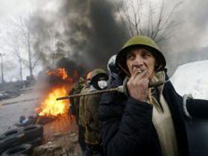 Un manifestante fuma un cigarrillo en las barricadas mientras contin&uacute;an los enfrentamientos con los antidisturbios en la Plaza de la Independencia en Kiev (Ucrania).