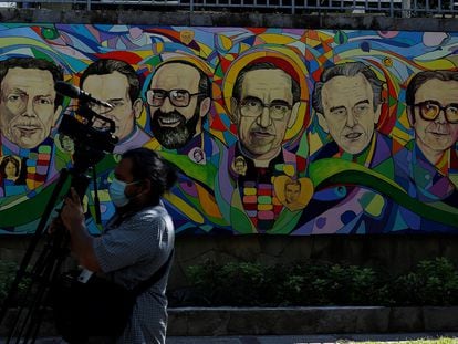 Un camarógrafo camina frente a una pintura dedicada a San Óscar Romero y seis sacerdotes jesuitas asesinados el 16 de noviembre de 1989 en San Salvador.