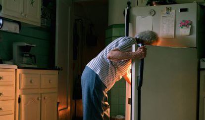Una mujer mayor mira en la nevera de su casa.