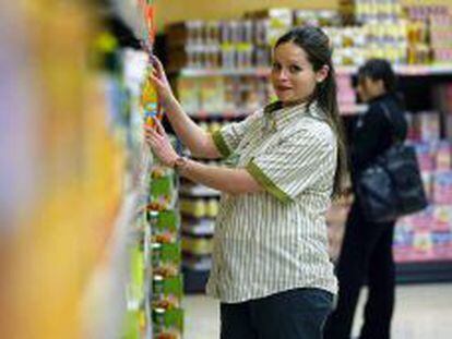 Una empleada embarazada de la cadena de supermercados Mercadona coloca art&iacute;culos en una estanter&iacute;a. 