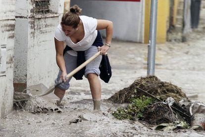 Una mujer de Aguilar de la Frontera trata de limpiar a paletadas la puerta de su casa después de las fuertes lluvias.