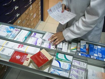 Una farmacéutica busca un medicamento en una estantería