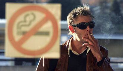Un hombre fuma en la calle frente a un cartel de prohibido