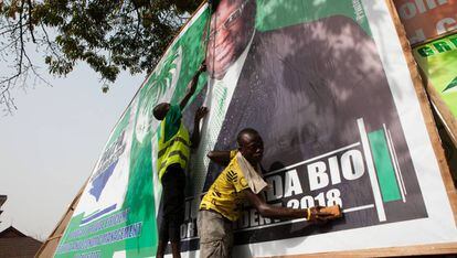 Dos chavales lavan el cartel electoral de Julius Maada Bio, candidato a la presidencia por el SLPP, en el Cotton Tree, uno de los lugares más simbólicos de la capital de Sierra Leona.