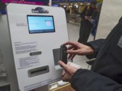 Una persona se identifica con su m&oacute;vil en un cajero autom&aacute;tico que dispensa bitcoines, en una tienda de discos.