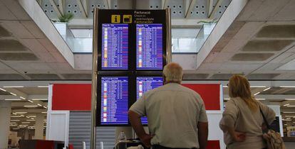 Dos turistas observan un panel de horarios en el aeropuerto de Palma de Mallorca.