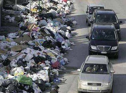 Automovilistas circulan ayer junto a bolsas de basura amontonadas en una calle de Nápoles.