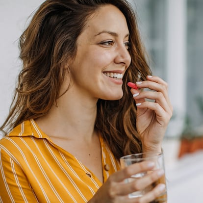 Mujer tomando un comprimido con un vaso de agua.