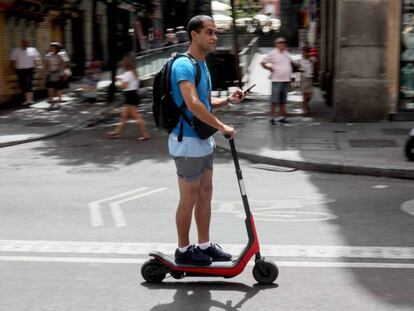 Un usuario conduce un patinete eléctrico por Madrid con el móvil en la mano.