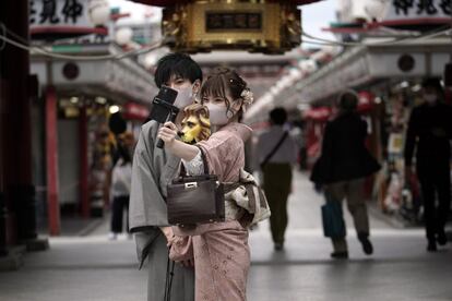 Visitantes protegidos con mascarillas se toman selfis en un centro comercial del distrito de Asakusa, en Tokio (Japón).