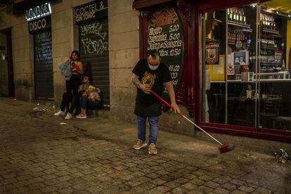 Un trabajador de un bar barre la puerta del negocio en el centro de Madrid.