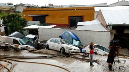 Un equipo de televisión filma unas casas y vehículos afectados por las fuertes lluvias en Aguilar de la Frontera.