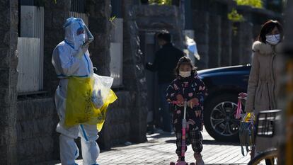 Una niña con mascarilla pasa junto a un trabajador que recoge muestra de control de la covid, este jueves en Pekín.