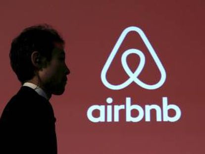 Un hombre camina frente al logo de la plataforma de alquiler de pisos Airbnb.