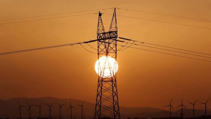 Torre de la línea eléctrica en primer plano y molinos de viento en el fondo.