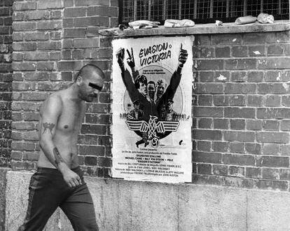 Un interno de la cárcel de Carabanchel de Madrid pasa ante un cartel de la película Evasión o victoria de John Huston, en el patio de la prisión, tras la fuga de dos reclusos.