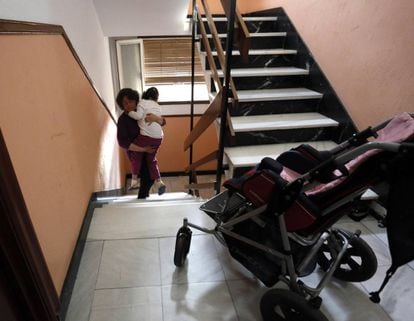 Una mujer sube en brazos a su hija con discapacidad a su casa en Madrid.