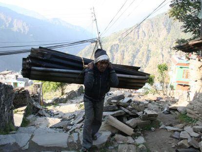 Un anciano carga con unas planchas de chapa para hacer el tejado de su casa en Dunche.