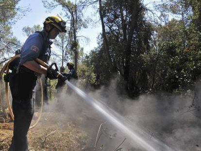 Un bombero remoja un &aacute;rea caliente del bosque afectado por el incendio de Madremanya.
