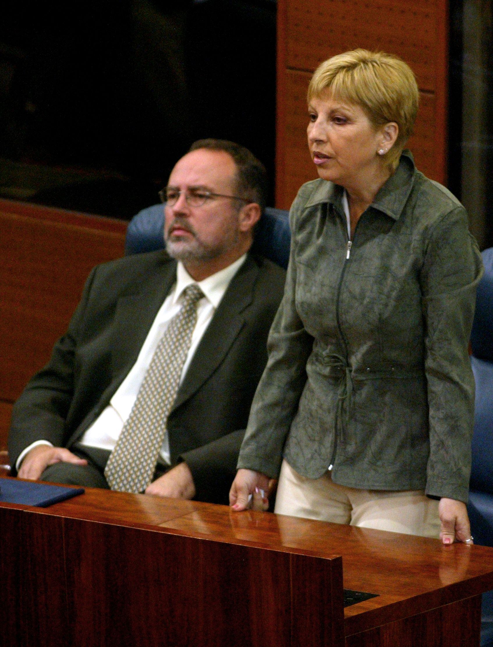Teresa Sáez vota de pie, junto a Eduardo Tamayo, sentado, en sus escaños de la Asamblea de Madrid.