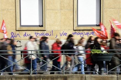 Los manifestantes caminandelante de un graffiti donde se lee: "fin del trabajo, la vida mágica" en la localidad de Rennes, Francia.