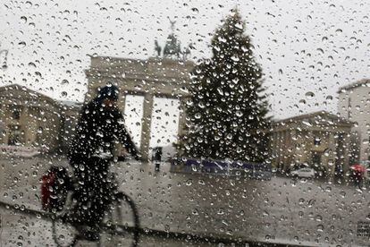 Una persona montando en bicicleta durante un día de lluvia frente a la Puerta de Branderburgo, en Berlín (Alemania).
