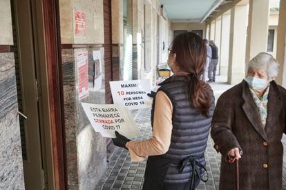 Una camarera coloca carteles de reducción de aforo y barra cerrada por la covid-19, en Pamplona.