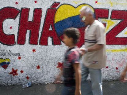 Dos transe&uacute;ntes caminan frente a un grafiti a favor de Ch&aacute;vez. 