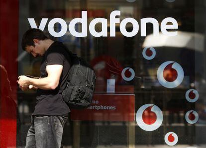 Un hombre consulta su tel&eacute;fono junto a una tienda de Vodafone.