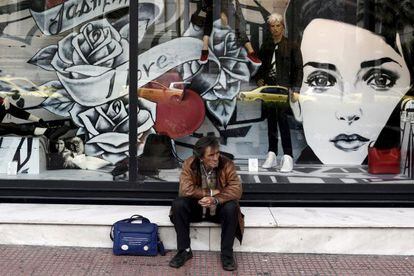 Un hombre sentado frente a una tienda en Atenas
