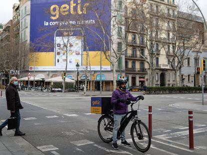 Un repartidor del supermercado en línea de entregas rápidas Getir ante una pancarta de la misma empresa, en Barcelona.