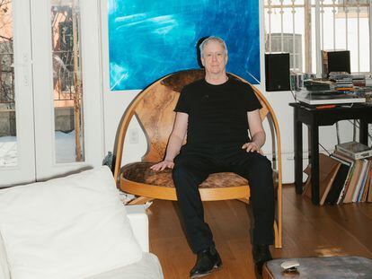 Tony Oursler, sentado en su salón en la silla que intercambió con su amigo el artista Richard Artschwager. En la pared, el espejo azul obra de Oursler.